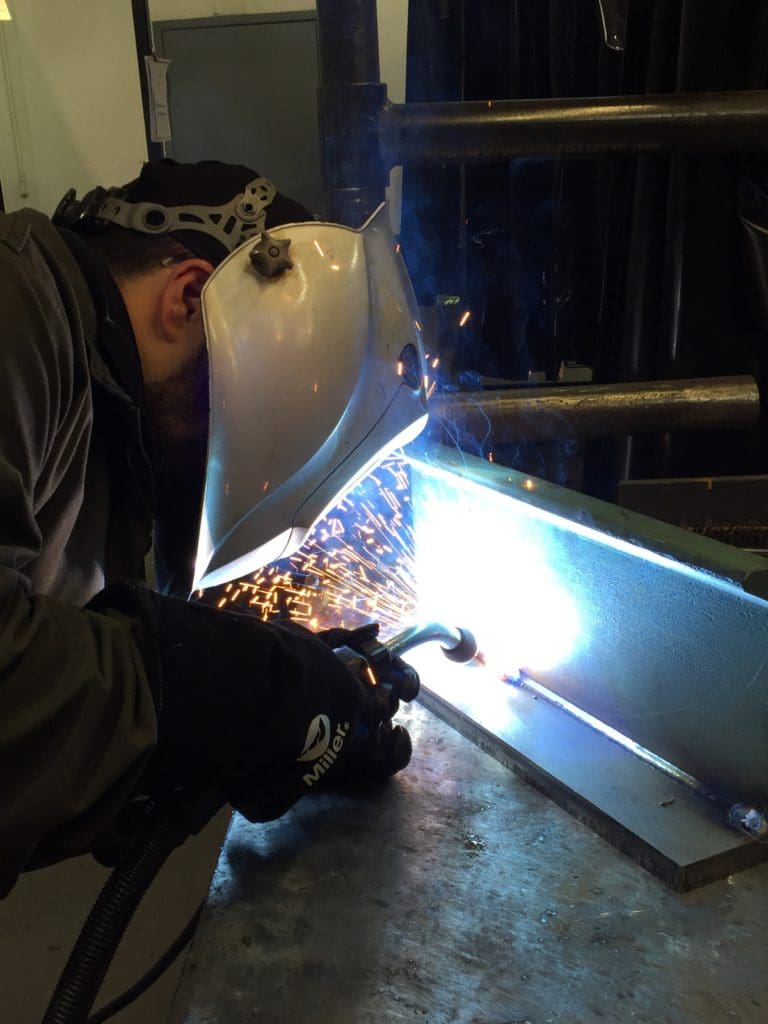 Closeup from the side of welding operator welding long part on a table