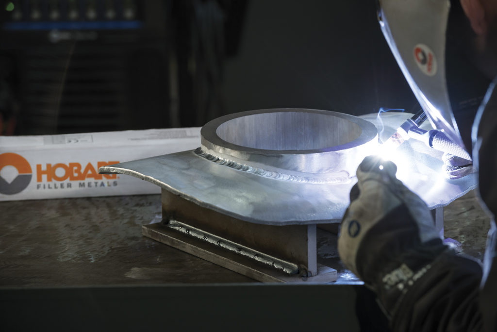 Closeup of welder TIG welding a circular piece of aluminum to a flat piece