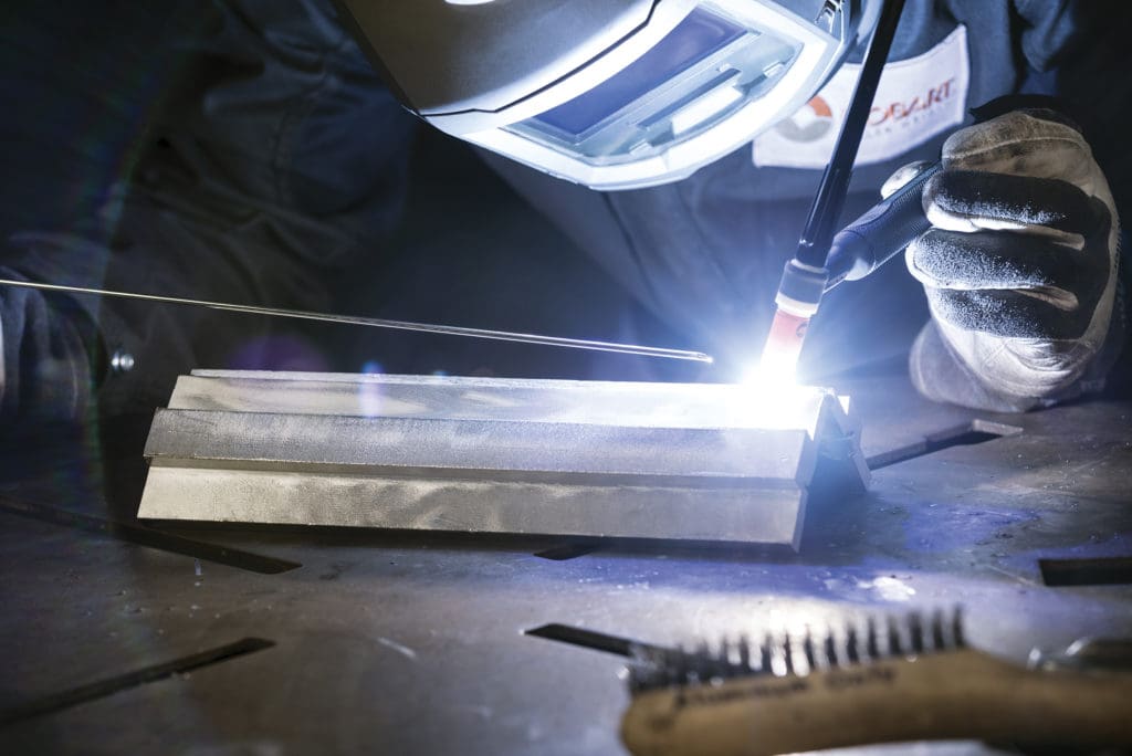 Closeup of welder TIG welding on an aluminum weld coupon