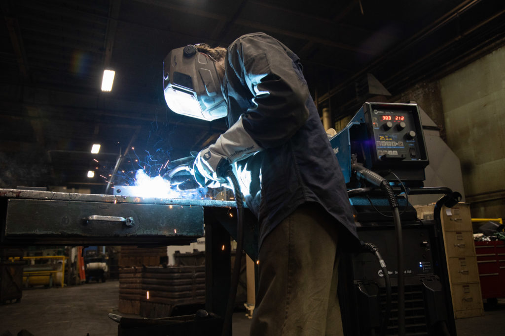 Side view of welding operator standing while welding a part on a table