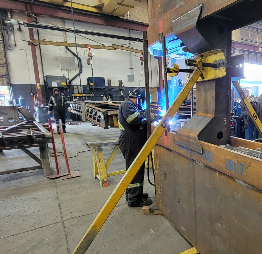 Side view of welder standing next to large component welding