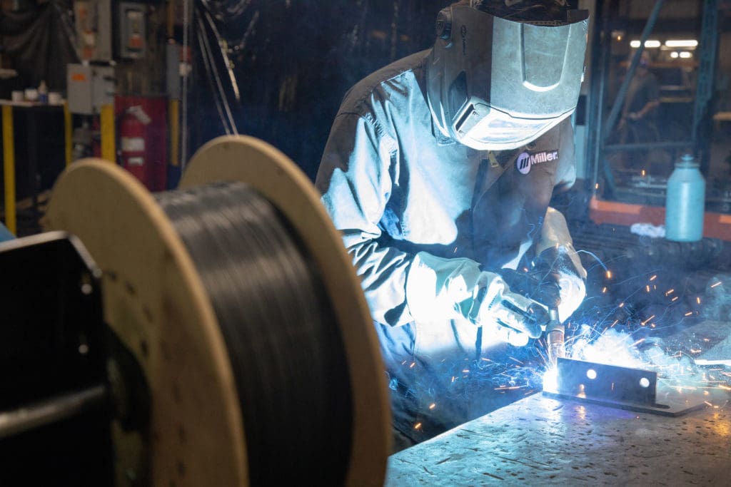 Welder welding part on table with spool in foreground