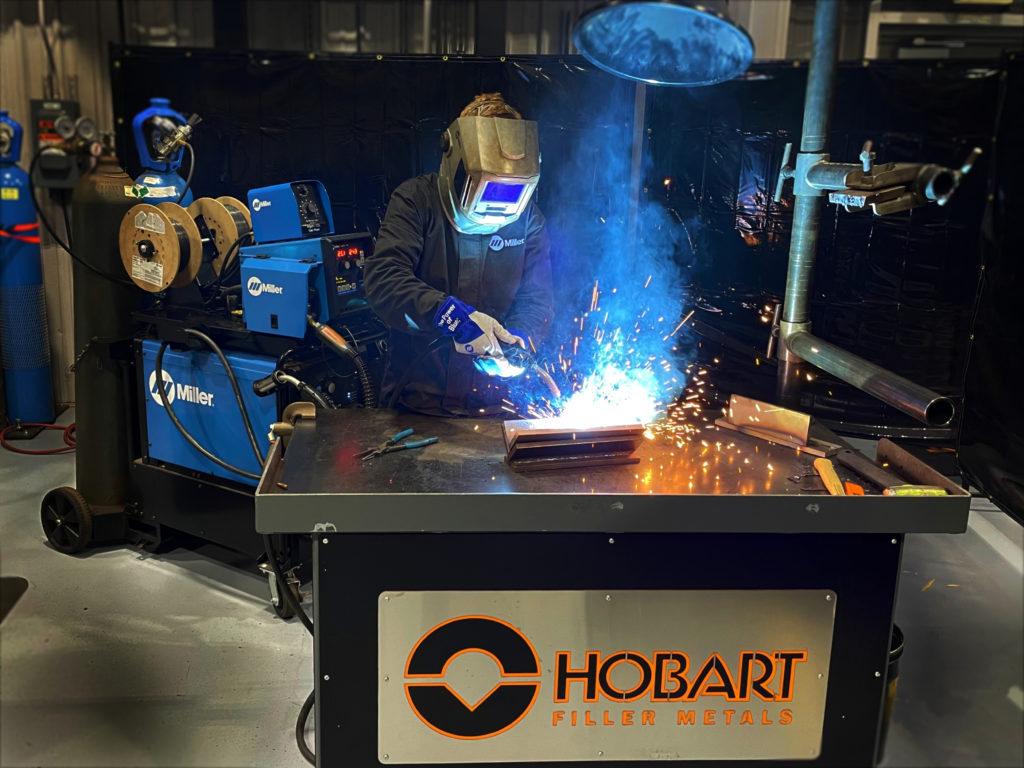 Welder welding coupon in flat/horizontal position on a Hobart workbench
