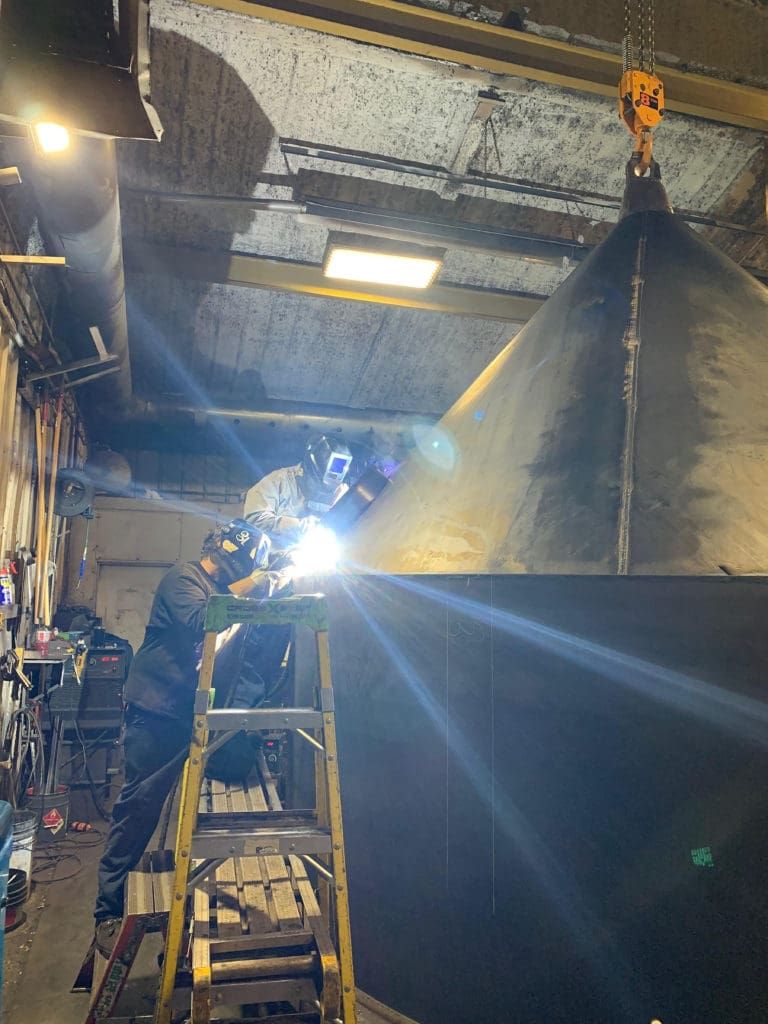 Side view of two welding operators welding on a large tank for concrete