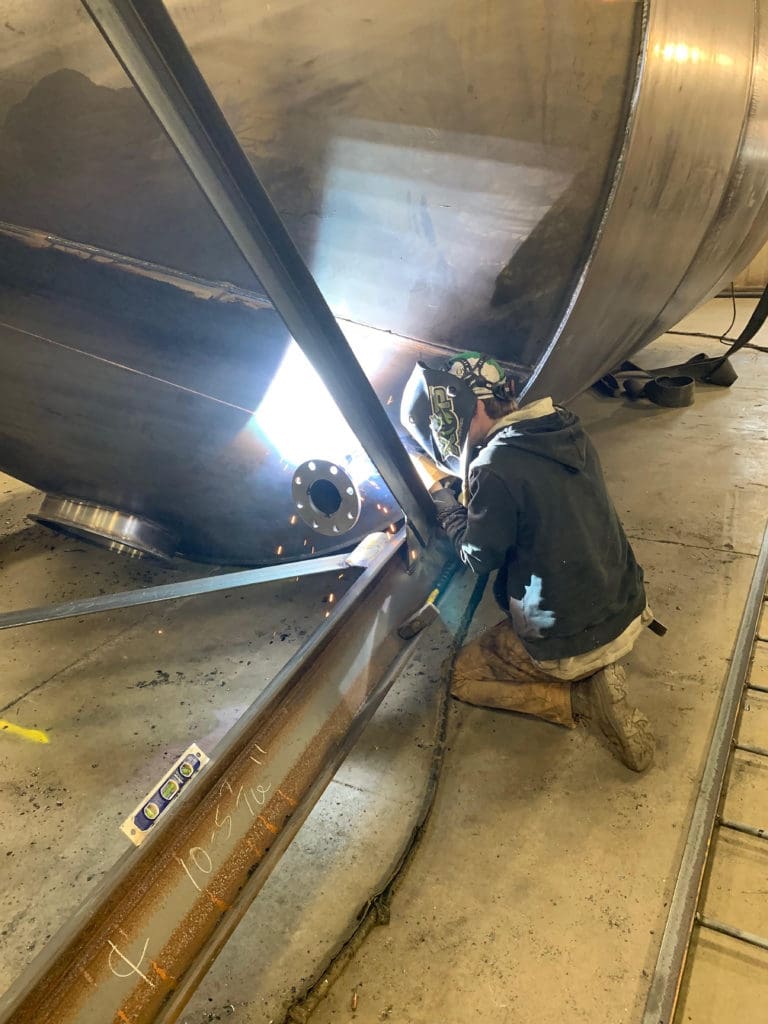 Welding operator kneeling on the floor welding on a large tank for concrete