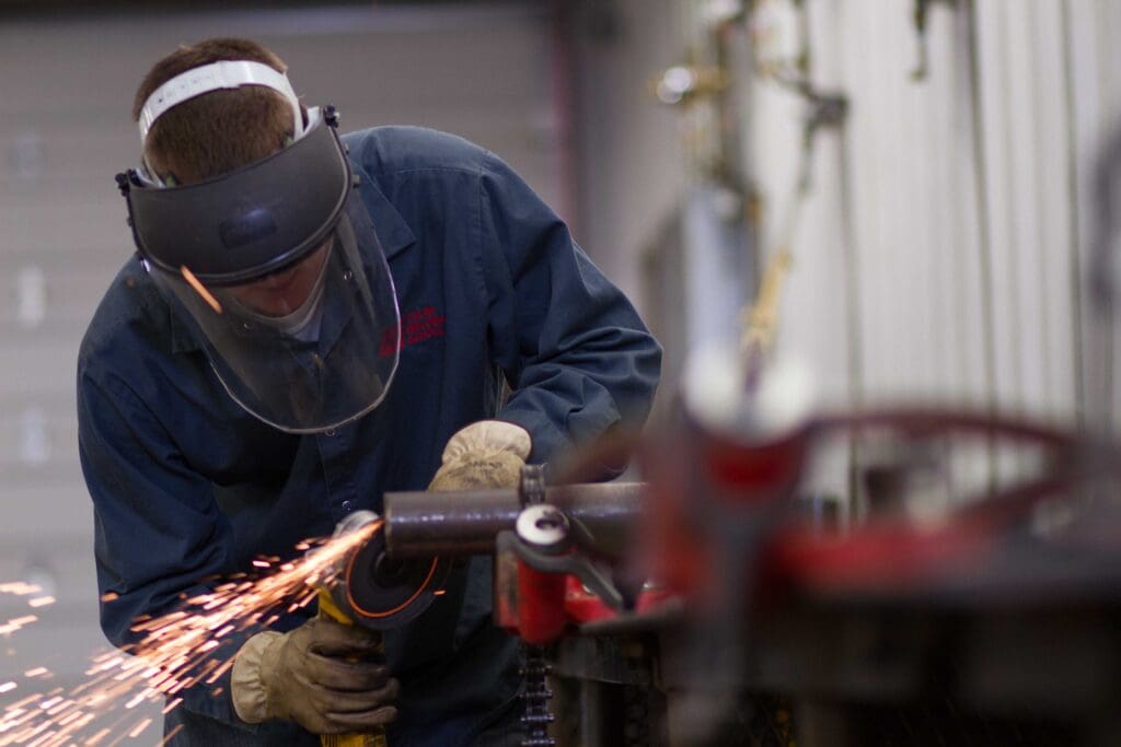 Welding student grinding a metal pipe clamped to a workbench